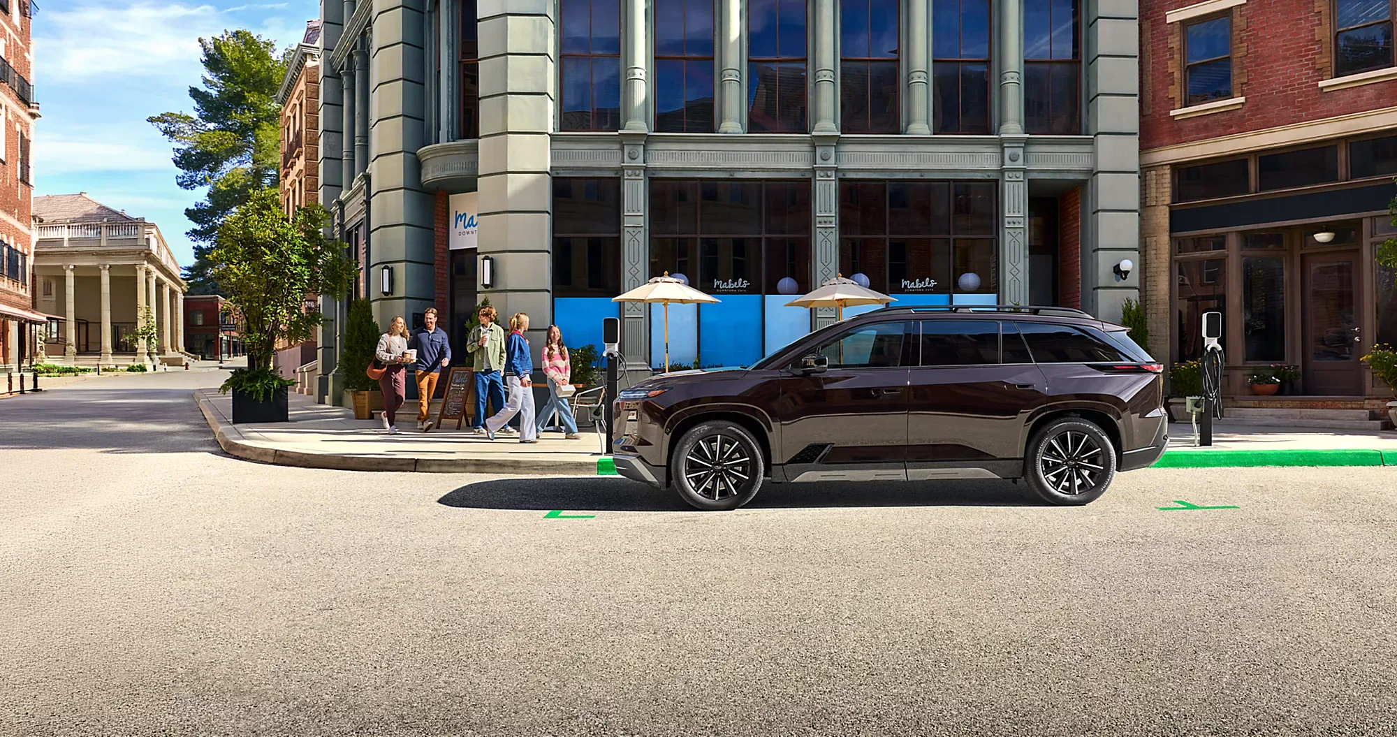 Side profile of the 2027 Subaru Getaway parked on a downtown street beside an EV charger.