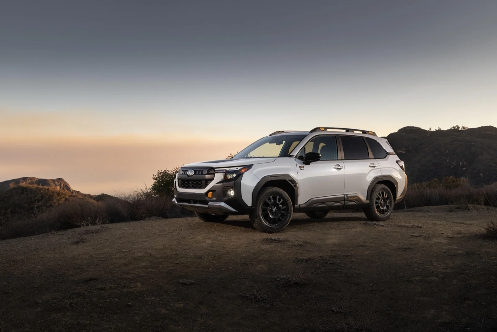 White 2026 Subaru Forester parked on a hilltop at dusk — Consumer Reports' Top Compact SUV for 2026