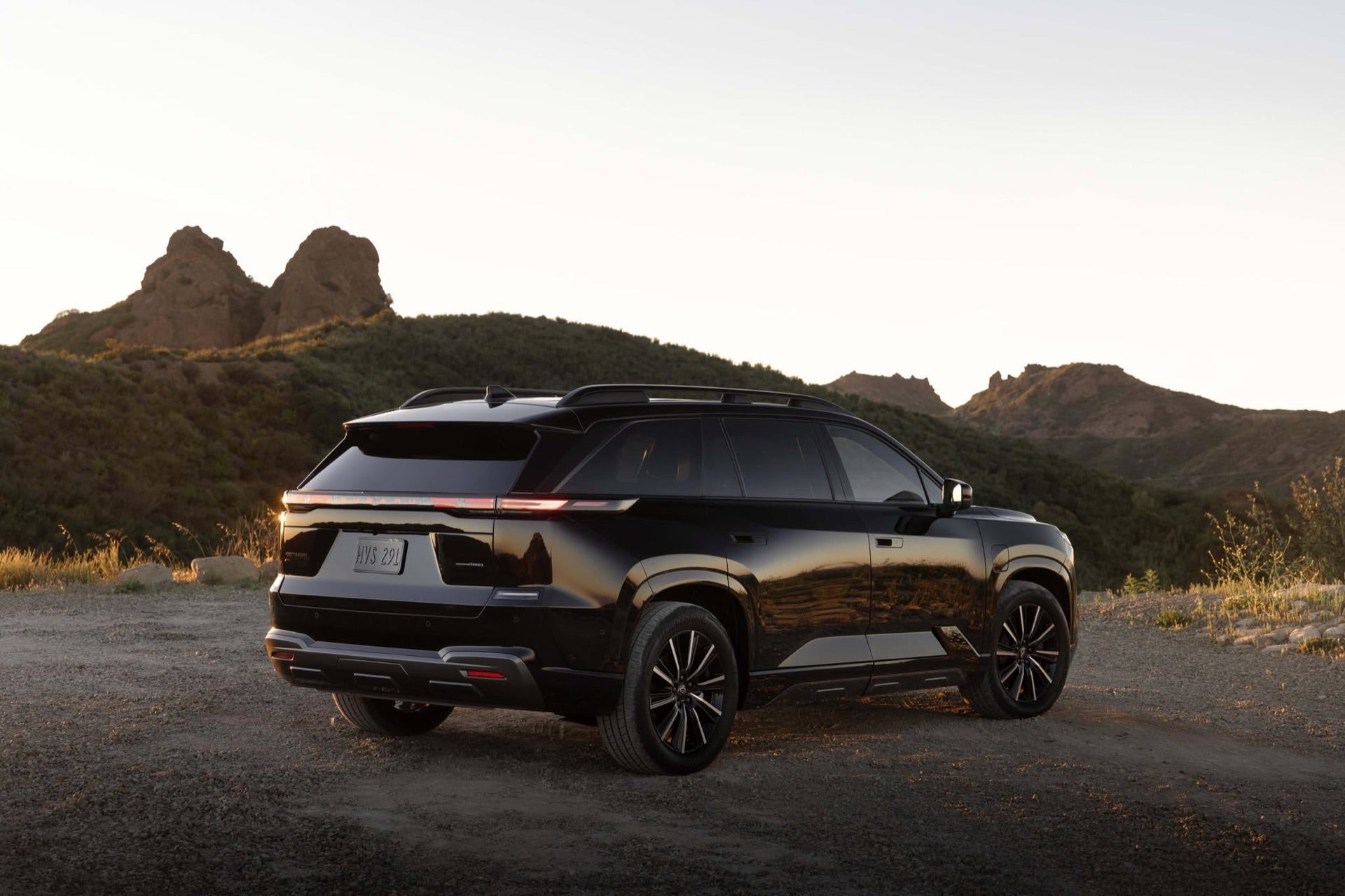 Rear three-quarter view of a black 2026 Subaru Outback parked on a dirt overlook at sunset.