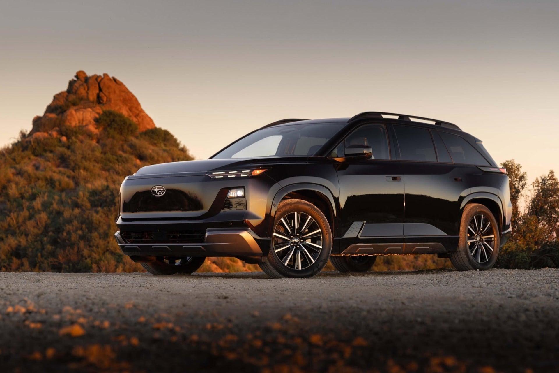 A black 2026 Subaru Outback parked on a dirt overlook at sunset, with a rocky hill behind it