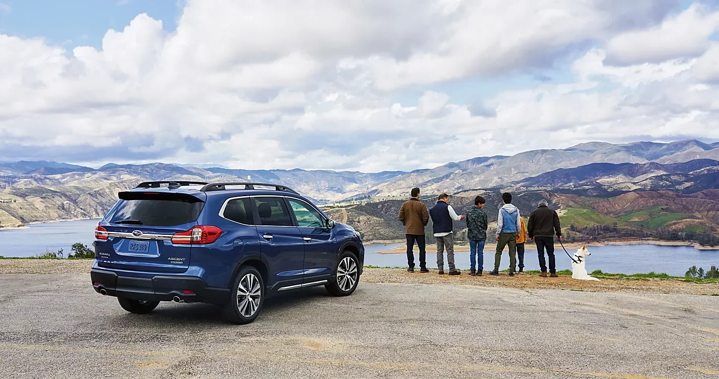A blue Subaru Ascent parked at a lake overlook while friends take in the view.