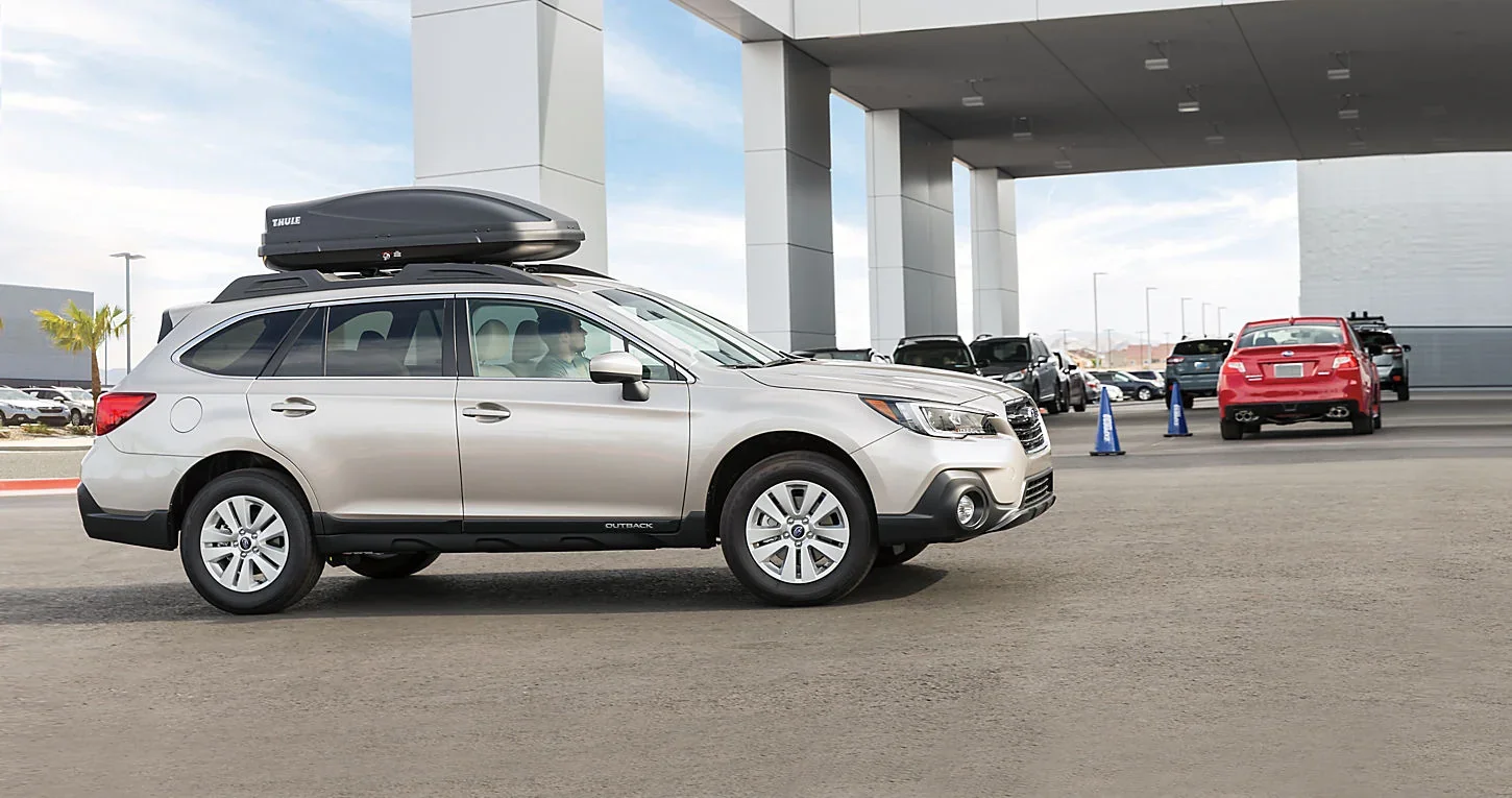 A silver Subaru Outback with a roof box parked outside the dealership.