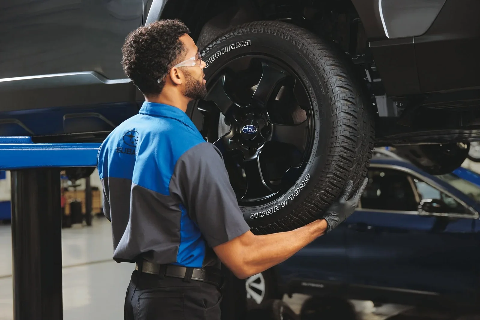 A technician lifting a wheel onto a raised Subaru.