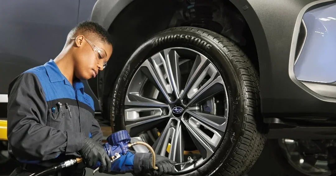 A technician tightening the wheel of a Subaru with an impact wrench.