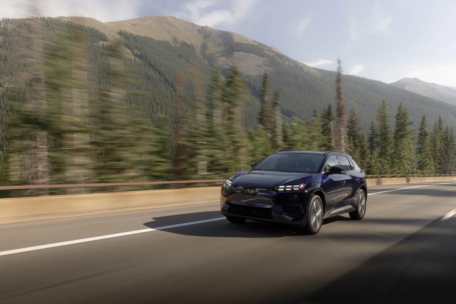 A dark blue Subaru Solterra driving through a mountain valley.